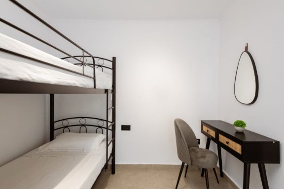 A minimalist bedroom with a bunk bed, desk, chair, and a mirror on the wall.