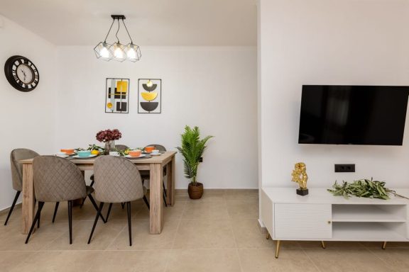 Modern dining area with a table, chairs, TV, and decorative plants. Bright and minimalist design.
