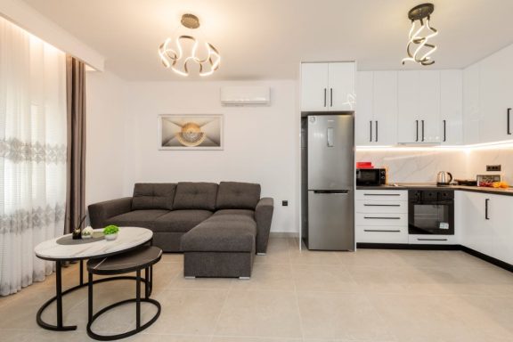 Modern living room with a grey sofa, coffee table, and kitchen area. Bright and minimalist design.