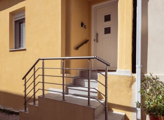 Yellow house exterior featuring steps and a railing leading to a white door.