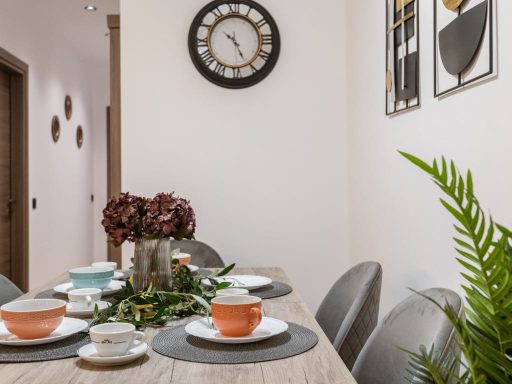 Dining table set with tableware, a clock on the wall, and decorative plants.