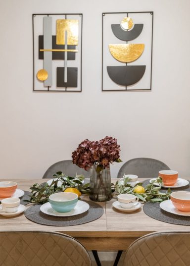 A dining table set with plates and bowls, decorated with flowers and wall art above.