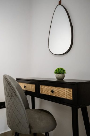 A minimalist desk with a chair, small plant, and an oval mirror on a light wall.